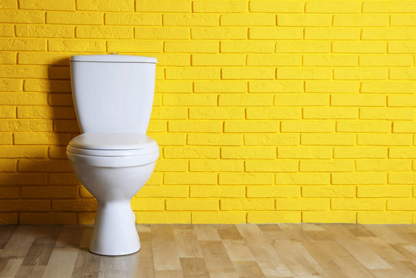 New clean toilet bowl near yellow brick wall indoors, space for text. Interior design - Photo, image