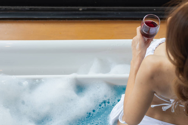 jonge vrouw heft glas rode wijn bij het zwembad in het resort waar ze genoten van haar verblijf om haar succesvolle bedrijf te vieren. jonge vrouw is het drinken van wijn om haar succesvolle zakelijke onderneming te vieren door het zwembad. - Foto, afbeelding