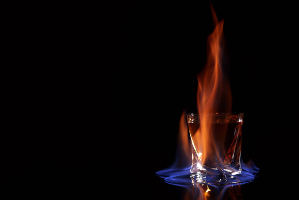 Glass with flaming vodka on black background, space for text - Фото, зображення