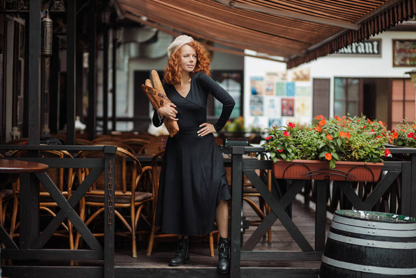 Eine Frau mit Baskenmütze und schwarzem Kleid hält ein Baguette in den Händen.  - Foto, Bild