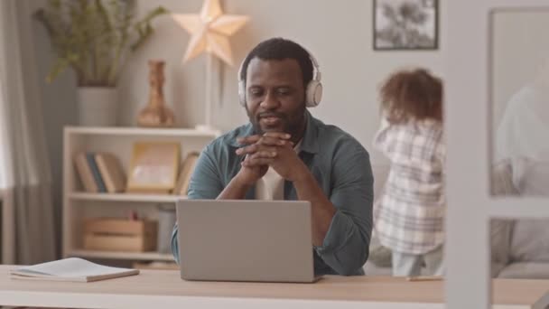 Media ripresa di uomo d'affari afro-americano in videoconferenza online su laptop mentre le sue due figlie birichine lo distraggono dal lavoro essendo rumoroso di proposito - Filmati, video