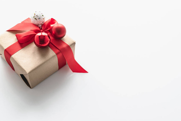 Χριστουγεννιάτικο δώρο σε συσκευασία χειροτεχνίας με κόκκινη κορδέλα και χριστουγεννιάτικες μπάλες. Εορταστική κάρτα με θέση για κείμενο. Οριζόντια φωτογραφία. - Φωτογραφία, εικόνα