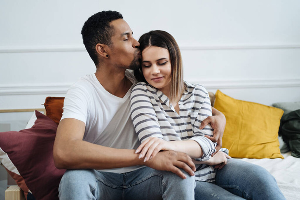 Front view of young diverse couple sitting on a couch at home - Photo, Image