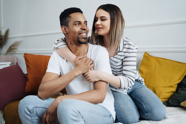 Front view of young diverse couple sitting on a couch at home - Photo, Image
