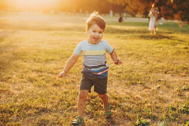 Caucasian boy runs along the field on camera. Childhood. Front view. Sunset. - Фото, изображение