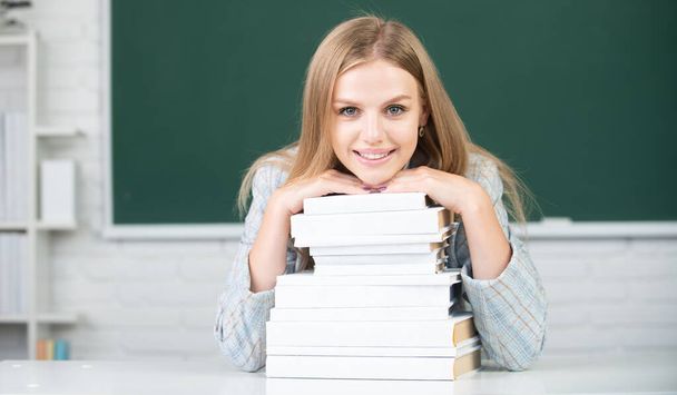 Student preparing exam and learning lessons in school classroom. Close up portrait of happy attractive young woman student with books on blackboard in classroom. - Foto, imagen