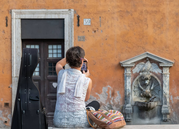Vrouw met Cello neemt foto van Italië historische drinkfontein spa draak in de buurt van Vaticaanstad Rome, Italië  - Foto, afbeelding