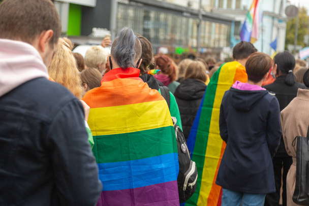 Οι άνθρωποι υποστηρίζουν την ΛΟΑΤΚΙ κοινότητα κατά τη διάρκεια της πορείας. Σημαίες Rainbow στους ώμους. - Φωτογραφία, εικόνα