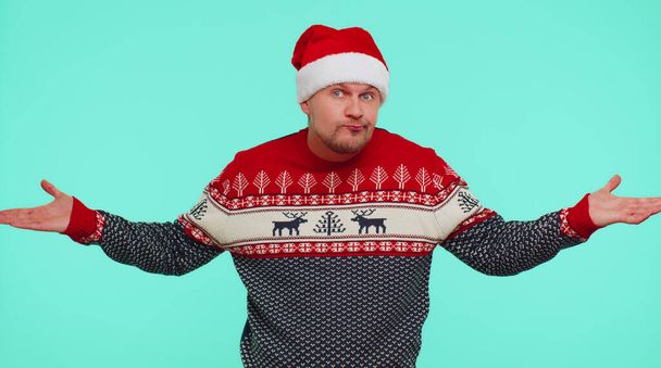 Μπερδεμένος άντρας με χριστουγεννιάτικο πουλόβερ που ντρέπεται για διφορούμενη ερώτηση που δεν έχει ιδέα - Φωτογραφία, εικόνα