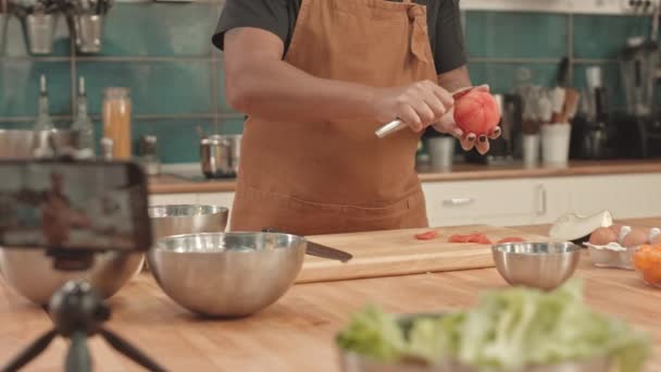 Low angle of cropped woman wearing apron, standing by table in professional kitchen, peeling tomatoes with knife - Footage, Video