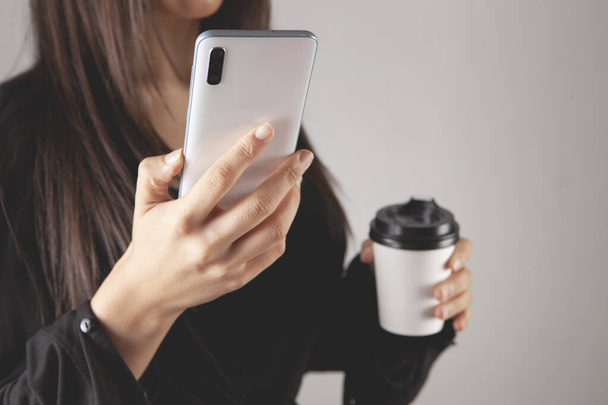 Elinde kahve ve telefon tutan genç bir kadın. - Fotoğraf, Görsel