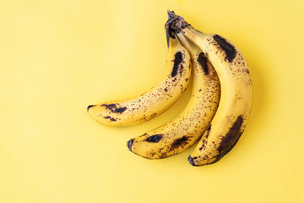 Three ripe bananas on a light yellow background. - Zdjęcie, obraz