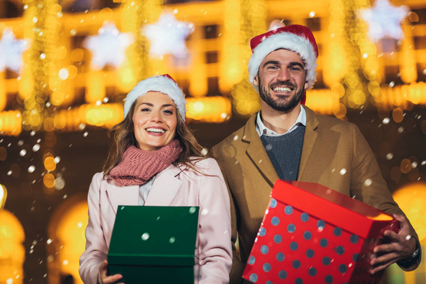 Joven pareja romántica sosteniendo caja de regalo divirtiéndose al aire libre en invierno antes de Navidad. - Foto, imagen