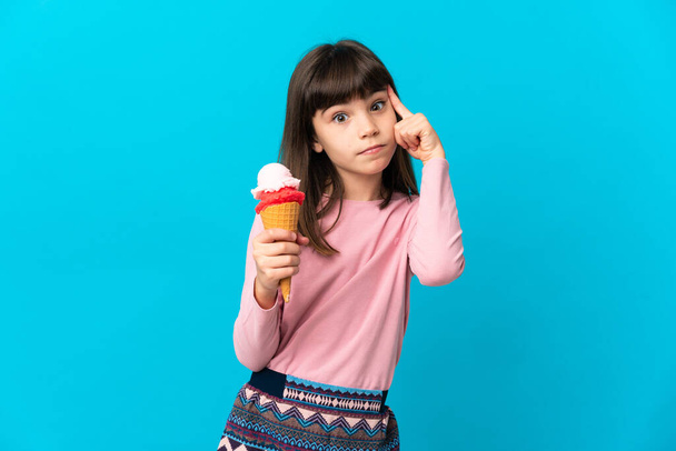 Petite fille avec une crème glacée cornet isolé sur fond bleu penser une idée - Photo, image