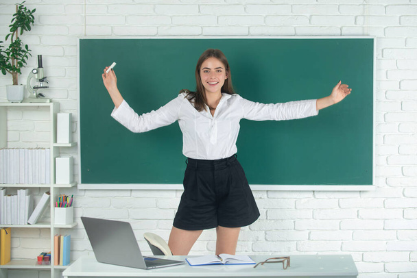 Female student excited amazet student with raised hands holding chalk at high school or college on blackboard background. - Fotó, kép