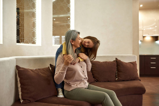 Beautiful granny is smiling while granddaughter is telling her something - Fotó, kép