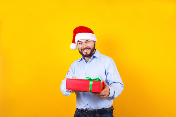 Retrato de un joven latino sosteniendo una caja de regalo de Navidad sobre un fondo amarillo en México - Foto, imagen