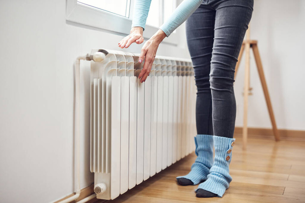 Woman heating her hands on the radiator during cold winter days. - Fotografie, Obrázek