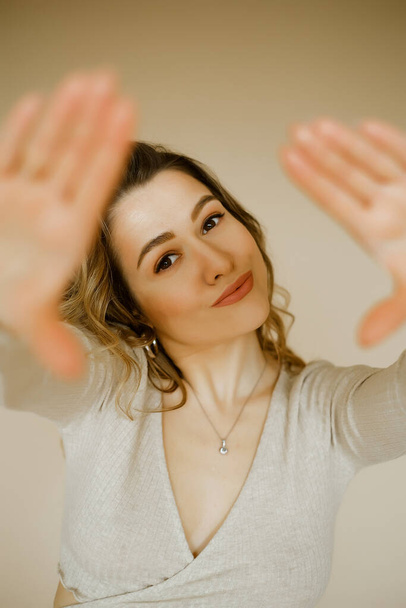 young caucaisan woman extends her arms out in front of her, beauty girl looks forward and puts her palms out, portrait of a young european lady at the beige wall, who puts her hands out in front of - 写真・画像