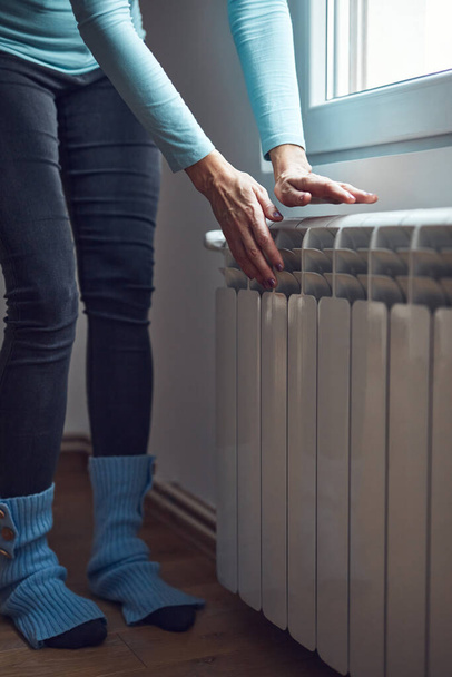 Mujer calentando sus manos en el radiador durante los fríos días de invierno. - Foto, imagen