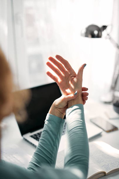 Femme avec douleurs aux mains, aux articulations, aux bras et aux doigts, étirements et massages pendant le travail sur un ordinateur portable. - Photo, image
