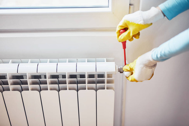 Handyman with gloves fixing and bleeding air from central heating gas radiator system at home. - Photo, Image