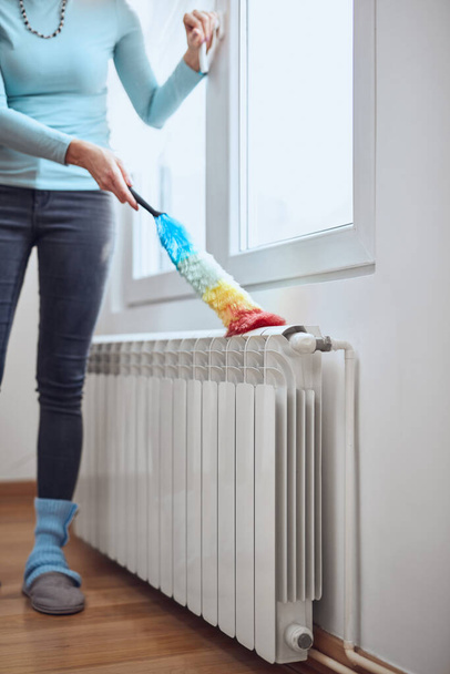 Femme avec un bâton de poussière nettoyage radiateur de gaz de chauffage central à la maison. - Photo, image