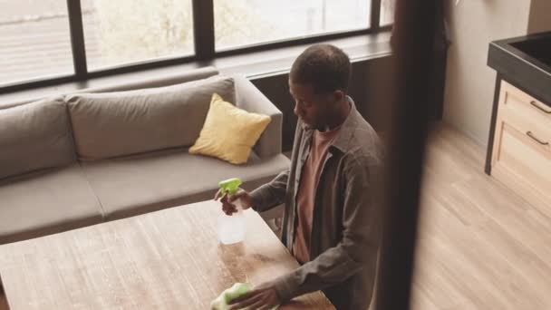 З-над-над уповільненої стрілянини молодого афро-американського чоловіка чистити поверхню дерев'яного кухонного столу виконуючи хатню роботу в його квартирі - Кадри, відео