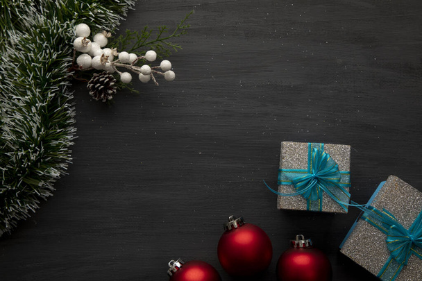 Kerstversiering op een zwarte achtergrond met rode bollen, geschenken en gouden welterusten - Foto, afbeelding