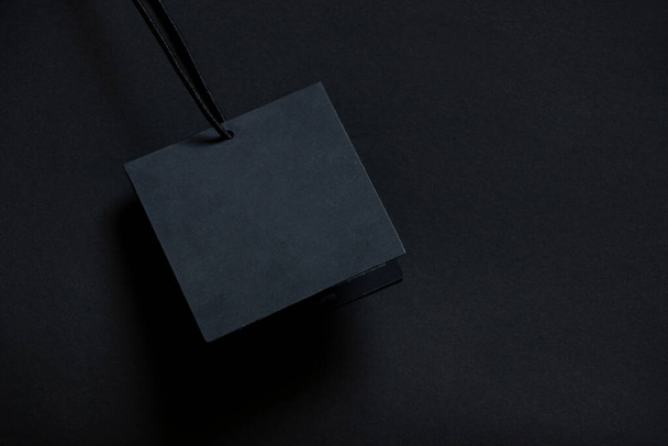 schwarze Papierkarte liegt auf schwarzem Hintergrund, leeres Papier auf einem Seil auf isoliertem Hintergrund, leerer Platz für das Preisschild - Foto, Bild