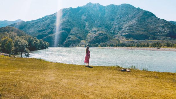 Lady in long red dress overlooks the edge of two rivers with mountains on the background. Drone footage - Photo, Image