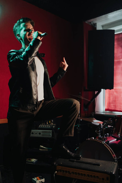Deri ceketli bir adam otantik bir stüdyoda karanlık bir yerde şarkı söylüyor. - Fotoğraf, Görsel