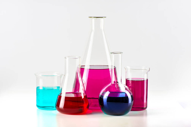 Le fiaschette da laboratorio con liquido colorato sono in fila su fondo bianco. Concetto di ricerca scientifica - Foto, immagini