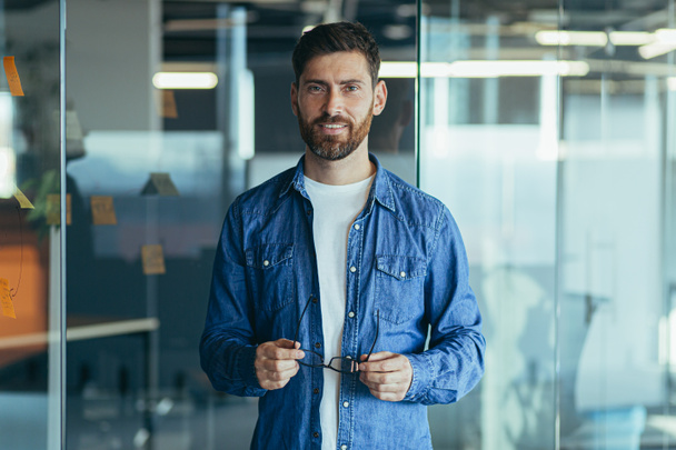 Šťastný vousatý podnikatel podnikatel startup majitel stojící v moderní kanceláři při pohledu do kamery, usmívající se mladý hipster, kreativní muž pózující na pracovišti, obchodní portrét - Fotografie, Obrázek