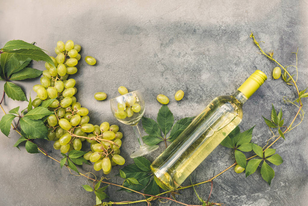 Вид сверху на белое вино, зеленую лозу, виноград и спелый виноград на винтажном фоне каменного стола. Винный магазин винный бар винный завод или дегустация вина концепции. - Фото, изображение