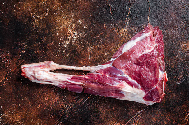 Nyers kecskelábú hús a csonton. Sötét háttér. Felülnézet - Fotó, kép