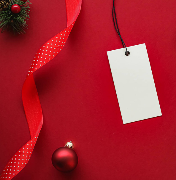Рождественская распродажа и праздничный дизайн. Чистый тег одежды и украшения Xmas и украшения на фоне красной бумаги, как плоский макет - Фото, изображение