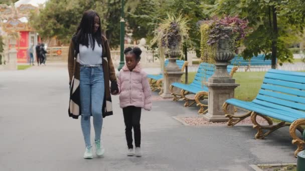 Giovane mamma che tiene la figlia a mano felice famiglia afro-americana che cammina nel parco della città bambino alzando la testa parlando con i genitori all'aperto bambina con la madre godere di conversazione mamma e bambino andando a casa - Filmati, video