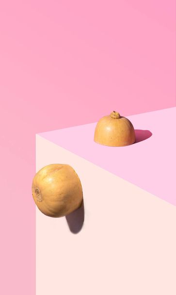 Organic fresh butter squash seats on the corner of the table. Pastel coral, pink and beige background. Still life abstract concept. - Photo, Image