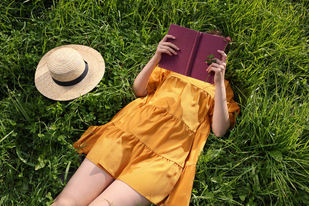 Woman reading book on green meadow, above view - Foto, afbeelding