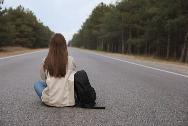 Young woman with backpack sitting on road near forest, back view - Foto, Imagem