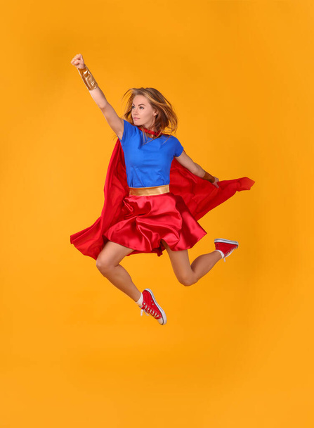 Confident woman in superhero costume jumping on yellow background - Photo, Image