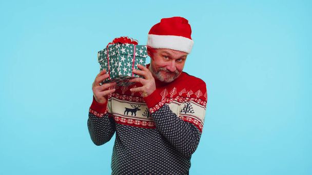 Komik adam Noel süveteri giyer, içinde hediyeler olan hediyelerle ilgilenir. - Fotoğraf, Görsel