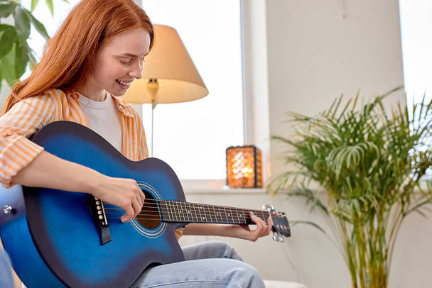 Portrait Of Young Redhead Female In Casual Wear Playing Guitar, At Home - Foto, imagen