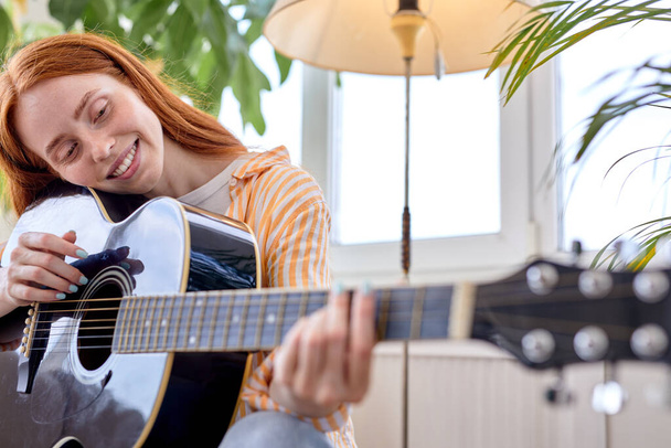 Adorable lady sit on sofa playing guitar, at home in cozy bright room, alone - Fotoğraf, Görsel