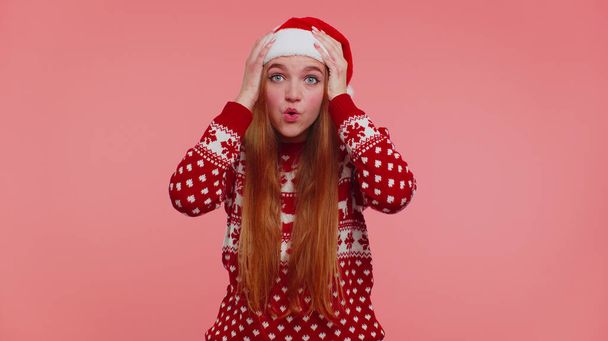 Взрослая девушка-подросток в рождественской шляпе поднимает руки в удивлении от внезапной победы, ничего себе эмоции - Фото, изображение