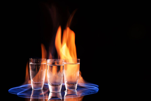 Vodka in shot glasses and flame on black background, space for text - Fotoğraf, Görsel