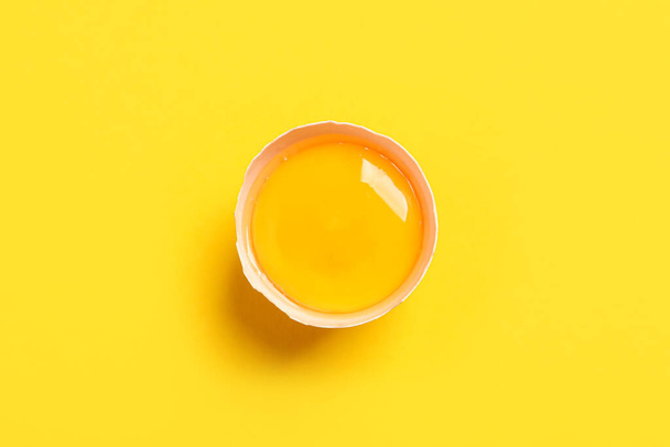 Cracked eggshell with raw yolk on yellow background, top view - Fotó, kép