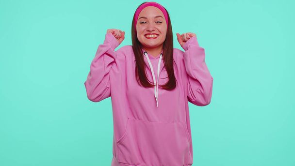 Teen girl in pink hoodie shouting, raising fists in gesture I did it, celebrating success, winning - Photo, Image