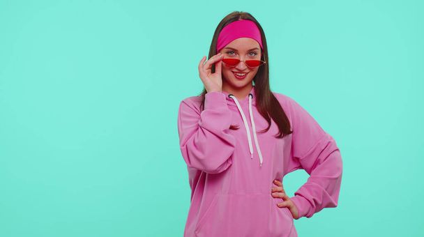 Verleidelijk vrolijk positief tiener meisje in hoodie dragen zonnebril, charmante glimlach, knipperend oog - Foto, afbeelding